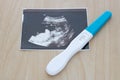 Pregnancy test showing a positive result and ultrasound picture of baby isolated on wooden background. Royalty Free Stock Photo