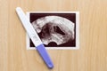 Pregnancy test with ultrasound picture of baby on wooden background. Pregnancy care concept. Royalty Free Stock Photo