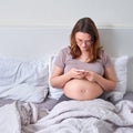 Pregnant adult woman with glasses looks at the phone for online consultation