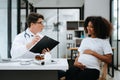 Pregnant african woman has appointment with doctor at clinic. Male gynaecologist OB GYN medic specialist with stethoscope listens