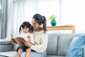 Pregnant Asian single mother is reading a book comfortably on her living room sofa. with a cute little daughter lying Royalty Free Stock Photo