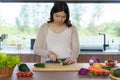 Pregnant Asian woman cutting cucumber for fresh green salad, female prepares tasty organic dinner at home, healthy nutrition for