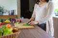 Pregnant Asian woman cutting cucumber for fresh green salad, female prepares tasty organic dinner at home, healthy nutrition for