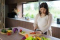 Pregnant Asian woman cutting tomato for fresh green salad, female prepares tasty organic dinner at home, healthy nutrition for Royalty Free Stock Photo