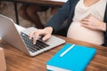 Pregnant attractive woman is typing on laptop keypad. Pregnancy in office.