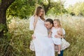 Pregnant beautiful mother and dad with little blonde girl in a white dress sitting on a swing, laughing, childhood, relaxation Royalty Free Stock Photo