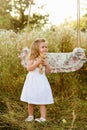Pregnant beautiful mother with little blonde girl in a white dress near a swing, laughing, childhood, relaxation Royalty Free Stock Photo