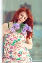 Pregnant beautiful red-haired woman sitting on a window sill at the window