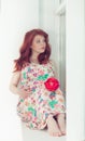 Pregnant beautiful red-haired woman sitting on a window sill at the window