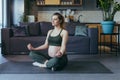 Pregnant beautiful woman doing yoga at home, sitting on a sports mat in the lotus position, closing her eyes, meditating Royalty Free Stock Photo