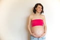 Pregnant belly on a light background. Smiling young pregnant jeans woman hugs her belly with her hands. The joy and