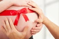 Pregnant belly with red ribbon and hands of mom and dad Royalty Free Stock Photo