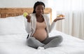 Pregnant black woman choosing between healthy and unhealthy food at home Royalty Free Stock Photo