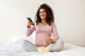 Pregnant black woman in pink shirt enjoying popcorn and holding remote controller Royalty Free Stock Photo
