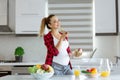 Pregnant blond young woman in red checkered shirt at kitchen eating a fruit salad, smiling, looking away, in front of Royalty Free Stock Photo