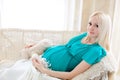 Pregnant blonde woman relaxing on sofa, reading book, dreaming, Royalty Free Stock Photo