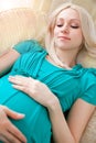 Pregnant blonde woman relaxing on sofa, reading book, dreaming, Royalty Free Stock Photo