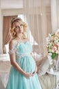 Pregnant bride blonde is preparing to become a mother and wife. Long turquoise dress on a girl body. Curly hair and a beautiful Royalty Free Stock Photo