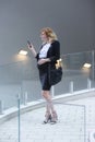 A pregnant businesswoman standing in front of the building and reading something on her mobile phone