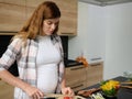 Pregnant Caucasian woman slicing tomatoes on a cutting board,preparing delicious healthy meal. A bow with a colorful healthy salad Royalty Free Stock Photo