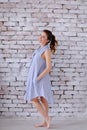 Pregnant caucasian woman wearing blue dress standing in brick wall background and holding belly.