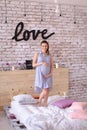 Pregnant charming woman wearing blue dress holding belly, inscription love on brick wall.