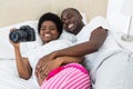 Pregnant couple lying on bed and looking photos in camera Royalty Free Stock Photo