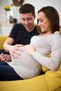 Pregnant Couple Sitting On Sofa With Man Touching Womans Stomach Royalty Free Stock Photo