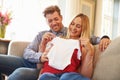 Pregnant Couple On Sofa At Home Looking At Baby Clothes Royalty Free Stock Photo