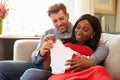 Pregnant Couple On Sofa At Home Looking At Baby Clothes Royalty Free Stock Photo