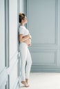 A pregnant European girl stands by the window