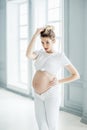 A pregnant European girl stands by the window