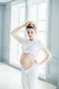 A pregnant European girl stands by the window