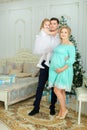 Pregnant european woman wearing blue dress standing with husband and little daughter near Christmas tree.