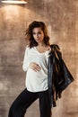 Pregnant european woman in white blouse and black pants in dark flat, stylish and happy pregnant woman in apartments