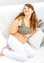 Pregnant female sitting on divan and eating pickle