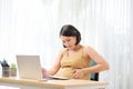 Pregnant freelancer touching belly near laptop