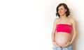 Pregnant gerl banner on a light background. Smiling young pregnant in jeans woman hugs her belly with her hands. The joy and