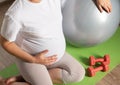 A pregnant girl with a big belly is engaged with dumbbells against the background of a gray fitball ball. Sports activities in the Royalty Free Stock Photo