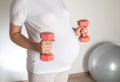 A pregnant girl with a big belly is engaged with dumbbells against the background of a gray fitball ball. Sports Royalty Free Stock Photo