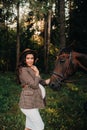 Pregnant girl with a big belly in a hat next to horses in the forest in nature.Stylish pregnant woman in the brown dress with the Royalty Free Stock Photo