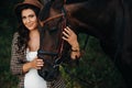 Pregnant girl with a big belly in a hat next to horses in the forest in nature.Stylish pregnant woman in the brown dress with the Royalty Free Stock Photo