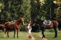 Pregnant girl with a big belly in a hat next to horses in the forest in nature.A stylish pregnant woman in a white dress and brown Royalty Free Stock Photo