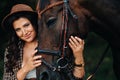 Pregnant girl with a big belly in a hat next to horses in the forest in nature.A stylish pregnant woman in a white dress and brown Royalty Free Stock Photo