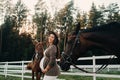 A pregnant girl with a big belly in a hat next to horses near a paddock in nature.Stylish pregnant woman in a brown dress with Royalty Free Stock Photo