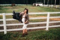 A pregnant girl with a big belly in a hat next to horses near a paddock in nature.Stylish pregnant woman in a brown dress with Royalty Free Stock Photo