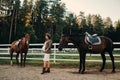 A pregnant girl with a big belly in a hat next to horses near a paddock in nature.Stylish pregnant woman in a brown dress with Royalty Free Stock Photo