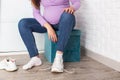 A pregnant girl with a big belly puts on sneakers on her feet. The concept of discomfort and inconvenience when bending over and
