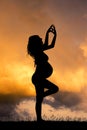 A pregnant girl doing yoga at sunset