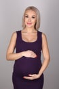 Pregnant girl in a dress hugging her belly. Close up. Gray background Royalty Free Stock Photo